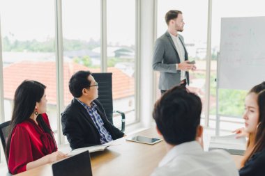 Genç iş adamları beyaz tahtadaki grafikleri ve istatistikleri açıklıyorlar. Toplantıya katılan şirket yöneticileri ve çalışanları.
