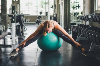 Spor tişörtü giyen güzel bir kadın lastik top, yoga ya da egzersiz topuyla esniyor ve dinleniyor..