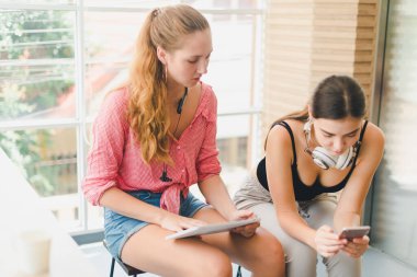 Telefon ve tablet oynayan iki güzel genç kadın. rahatlama konsepti.