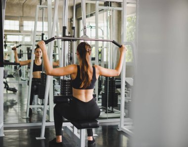Spor salonunda kol ve omuz kaslarıyla oynamak için bir çekme makinesiyle egzersiz yapan güzel bir sporcu. Spor konsepti alıştırması.