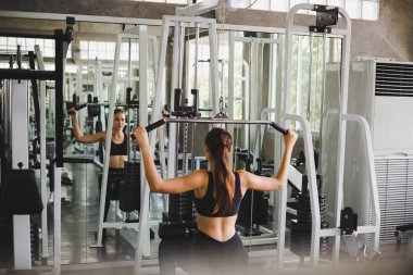 Spor salonunda kol ve omuz kaslarıyla oynamak için bir çekme makinesiyle egzersiz yapan güzel bir sporcu. Spor konsepti alıştırması.