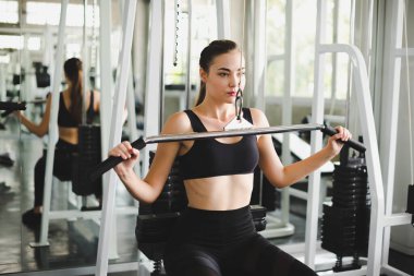 Spor salonunda kol ve omuz kaslarıyla oynamak için bir çekme makinesiyle egzersiz yapan güzel bir sporcu. Spor konsepti alıştırması.