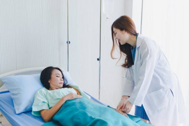 Asyalı kadın doktor hastane yatağında yatan hastayı ziyaret ediyor..