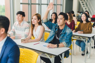 Asyalı erkek konuşmacı seminerlerde ve atölyelerde toplantıdaki insanlarla konuşuyor. Toplantıya katılanlar soru sormak için ellerini kaldırdılar..