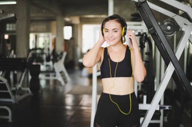 Güzel kadınlar spor salonuna egzersiz yapmaya gelir ve kulaklıklardan müzik dinleyerek rahatlarlar. Spor giyer..