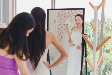 Nedime, güzel geline aynanın önünde beyaz bir gelinlik giymesinde yardım ediyor..