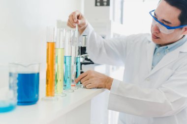 Asyalı bilim adamları laboratuvarda test ve analiz için kimyasallar hazırlıyorlar. Bilim adamları cam ve beyaz gömlekleri temizliyorlar. Bilim ve Kimya Konsepti