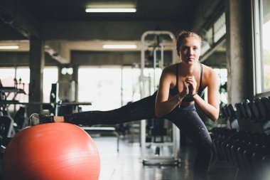 Spor tişörtü giyen güzel bir kadın lastik top, yoga ya da egzersiz topuyla esniyor ve dinleniyor..