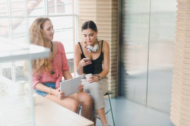 Kahve içip telefonla oynayan iki güzel genç kadın. rahatlama konsepti.