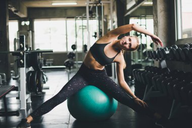 Spor tişörtü giyen güzel bir kadın lastik top, yoga ya da egzersiz topuyla esniyor ve dinleniyor..