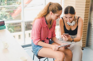 Telefon ve tablet oynayan iki güzel genç kadın. rahatlama konsepti.