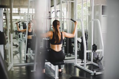 Spor salonunda kol ve omuz kaslarıyla oynamak için bir çekme makinesiyle egzersiz yapan güzel bir sporcu. Spor konsepti alıştırması.