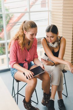 Telefon ve tablet oynayan iki güzel genç kadın. rahatlama konsepti.