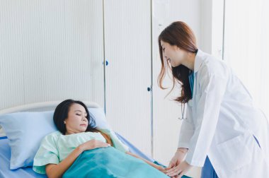 Asyalı kadın doktor hastane yatağında yatan hastayı ziyaret ediyor..