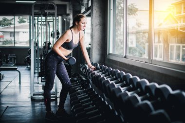 Güzel bayan sporcular spor salonunda egzersiz yapıyorlar. Dambılı kaldırarak. Spor salonunda bir sürü egzersiz malzemesi var..