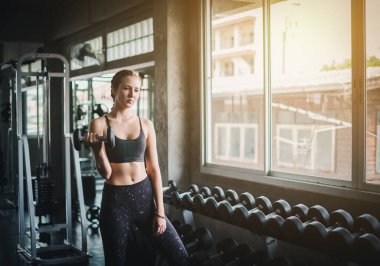 Güzel bayan sporcular spor salonunda egzersiz yapıyorlar. Dambılı kaldırarak. Spor salonunda bir sürü egzersiz malzemesi var..