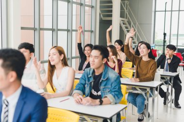 Asyalı erkek konuşmacı seminerlerde ve atölyelerde toplantıdaki insanlarla konuşuyor. Toplantıya katılanlar soru sormak için ellerini kaldırdılar..
