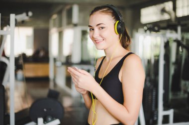 Güzel kadınlar spor salonuna egzersiz yapmaya gelir ve kulaklıklardan müzik dinleyerek rahatlarlar. Spor giyer..