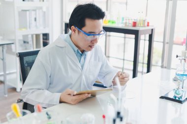 Asyalı bilim adamları laboratuvarda test ve analiz için kimyasallar hazırlıyorlar. Bilim adamları cam ve beyaz gömlekleri temizliyorlar. Bilim ve Kimya Konsepti
