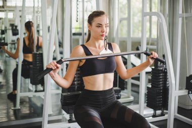 Spor salonunda kol ve omuz kaslarıyla oynamak için bir çekme makinesiyle egzersiz yapan güzel bir sporcu. Spor konsepti alıştırması.