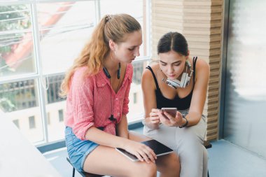 Telefon ve tablet oynayan iki güzel genç kadın. rahatlama konsepti.
