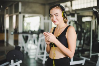 Güzel kadınlar spor salonuna egzersiz yapmaya gelir ve kulaklıklardan müzik dinleyerek rahatlarlar. Spor giyer..