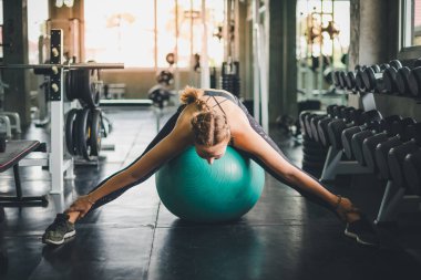 Spor tişörtü giyen güzel bir kadın lastik top, yoga ya da egzersiz topuyla esniyor ve dinleniyor..