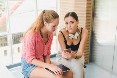 Telefon ve tablet oynayan iki güzel genç kadın. rahatlama konsepti.