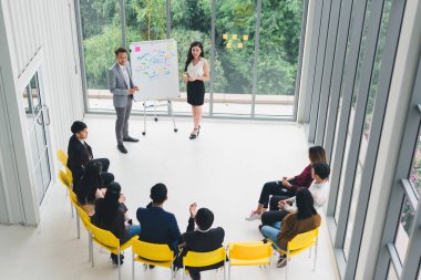 Seminerlerde ve atölyelerde toplantıdaki insanlara konuşan Asyalı erkek ve kadın konuşmacı. Yarı daire etrafında oturan seminer ve eğitimin katılımcıları tarafından. Üst görünüm.