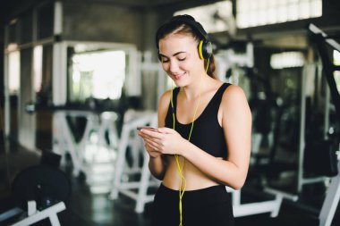 Güzel kadınlar spor salonuna egzersiz yapmaya gelir ve kulaklıklardan müzik dinleyerek rahatlarlar. Spor giyer..