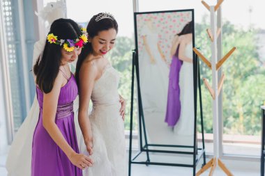 Nedime, güzel geline aynanın önünde beyaz bir gelinlik giymesinde yardım ediyor..