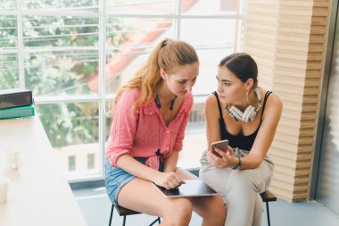 Telefon ve tablet oynayan iki güzel genç kadın. rahatlama konsepti.