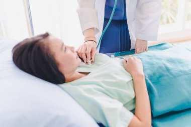 Asyalı kadın doktor hastanın nefes alan stetoskoplarını inceledi. Hastanın yatağında yatıyor..