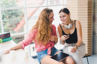 Telefon ve tablet oynayan iki güzel genç kadın. rahatlama konsepti.