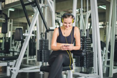 Güzel kadınlar spor salonuna egzersiz yapmaya gelir ve kulaklıklardan müzik dinleyerek rahatlarlar. Spor giyer..