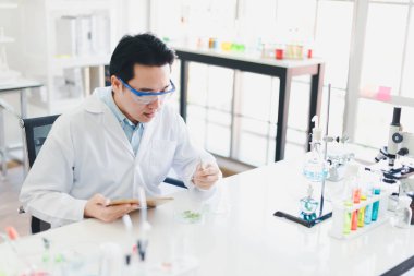 Asyalı bilim adamları laboratuvarda test ve analiz için kimyasallar hazırlıyorlar. Bilim adamları cam ve beyaz gömlekleri temizliyorlar. Bilim ve Kimya Konsepti