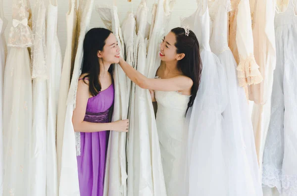 Bride and Bridesmaid Is choosing the bride\'s dress in the shop to put on his upcoming wedding. Valentines Day Love Concept.