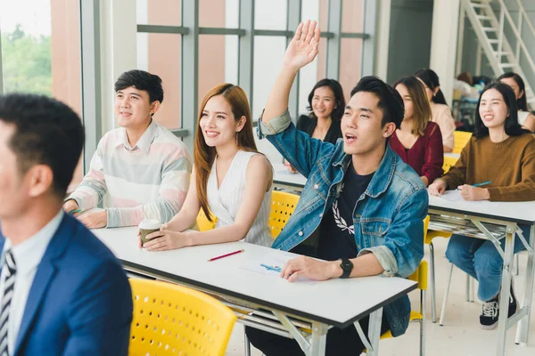 Asian male speaker is speaking at seminars and workshops to the people in the meeting. Those attending the meeting raised their hands to ask questions.