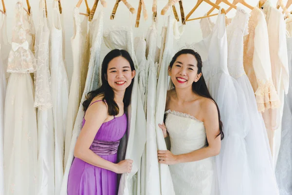 Bride and Bridesmaid Is choosing the bride\'s dress in the shop to put on his upcoming wedding. Valentines Day Love Concept.