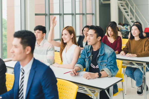 Asian male speaker is speaking at seminars and workshops to the people in the meeting. Those attending the meeting raised their hands to ask questions.