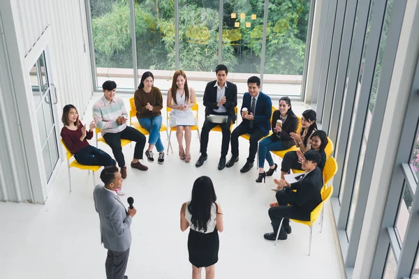 Seminerlerde ve atölyelerde toplantıdaki insanlara konuşan Asyalı erkek ve kadın konuşmacı. Yarı daire etrafında oturan seminer ve eğitimin katılımcıları tarafından. Üst görünüm.
