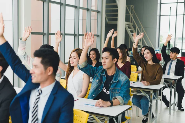 Asyalı erkek konuşmacı seminerlerde ve atölyelerde toplantıdaki insanlarla konuşuyor. Toplantıya katılanlar soru sormak için ellerini kaldırdılar..