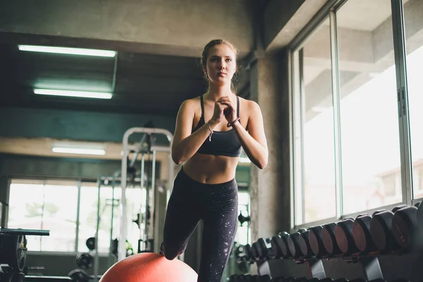 Spor tişörtü giyen güzel bir kadın lastik top, yoga ya da egzersiz topuyla esniyor ve dinleniyor..