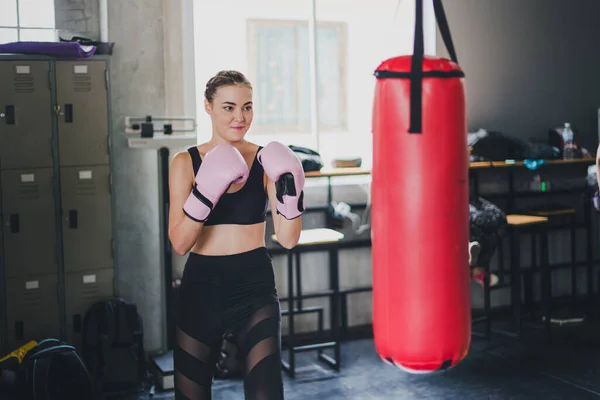 Beautiful fitness boxing gym. She wears a pink boxing glove and wears exercise. Sandbag is a pair of punches.