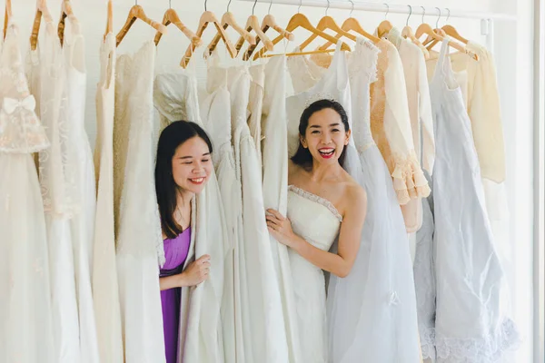 Bride and Bridesmaid Is choosing the bride\'s dress in the shop to put on his upcoming wedding. Valentines Day Love Concept.