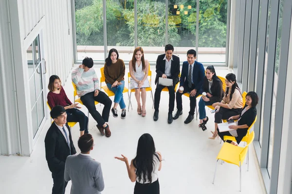 Seminerlerde ve atölyelerde toplantıdaki insanlara konuşan Asyalı erkek ve kadın konuşmacı. Yarı daire etrafında oturan seminer ve eğitimin katılımcıları tarafından. Üst görünüm.