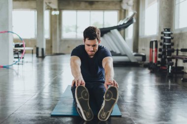 Spor salonunda yoga minderleri üzerinde egzersiz yapmadan önce esneme hareketleri yapan atletik erkekler. Kolları kasılmış..