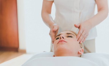 Lüks kaplıcalarda spa masajı ve rahatlama için yatakta uzanan güzel bir kadın. Masör yüzüne ve kafasına spa odasında masaj yaptı..