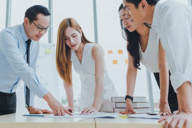 Asyalı takım arkadaşları grafikler ve iş gazetelerinin çalışmalarını tartışmak için toplanıyorlar..