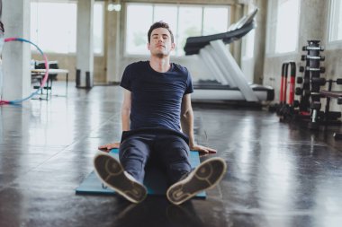 Spor salonunda yoga minderleri üzerinde egzersiz yapmadan önce esneme hareketleri yapan atletik erkekler. Boyun kaslarını esneterek..